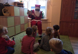 Dzieci siedzą na dywanie, Mikołaj czyta im książeczkę